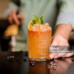 Bartender finished decorating his cocktail with mint and orange slice